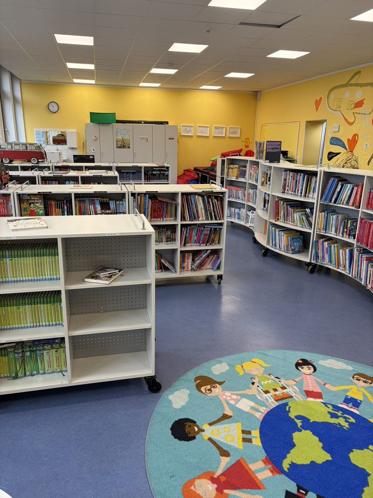 Schulbücherei mit Bücherregalen und einem runden Weltteppich